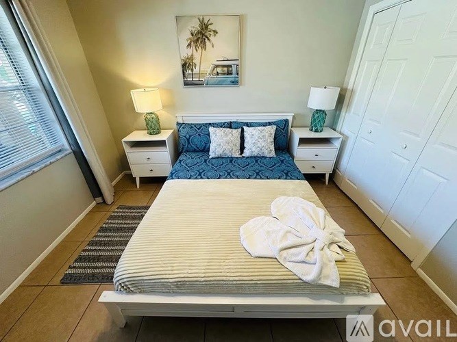 A bedroom with a bed, nightstands, and a painting of a beach scene.