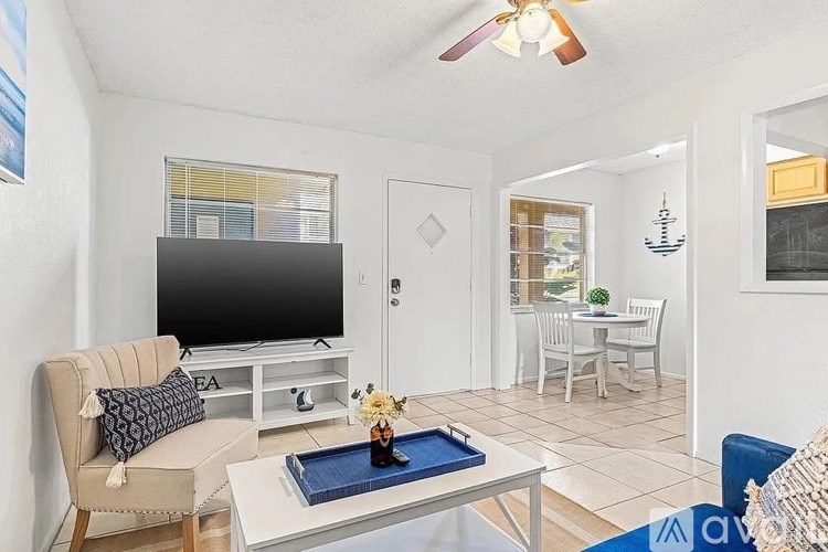 A living room with a television, a chair, a coffee table, and a dining area in the background.