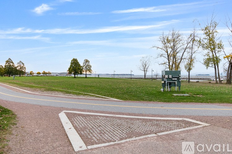A park with a paved path and a bench overlooking a body of water.