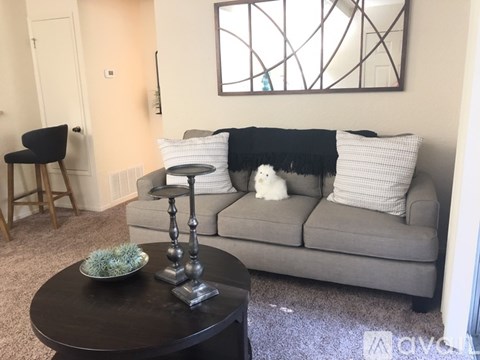 A living room with a grey couch, a black table, and a white cat.