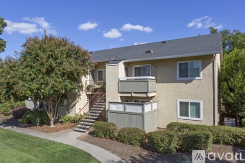 A beige apartment building with a front lawn and trees.