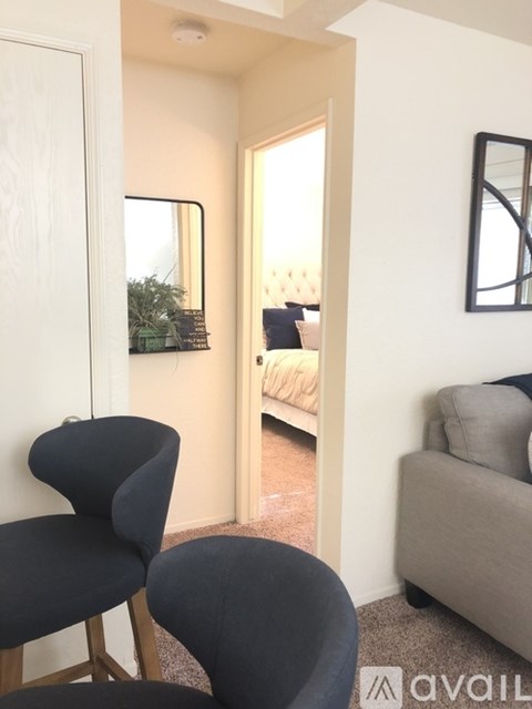 A living room with a grey couch, a black chair and a mirror on the wall.