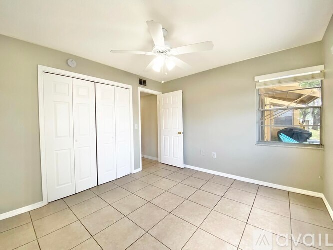 A room with a ceiling fan and a window with a view of a pool.