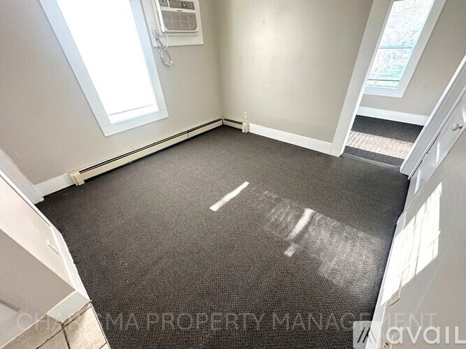 A room with a carpeted floor and a window letting in sunlight.