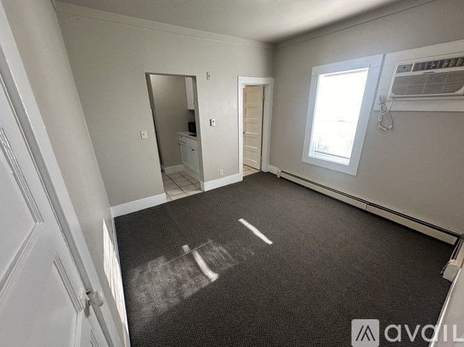 A room with a carpeted floor, a door, a window, and a wall-mounted air conditioner unit.
