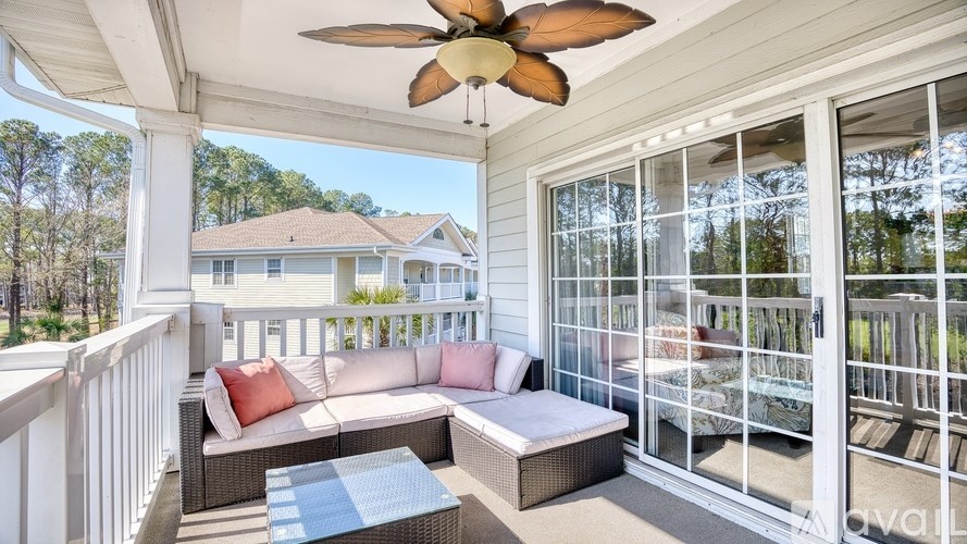 A patio with a white railing, a sofa, a coffee table, and a ceiling fan.