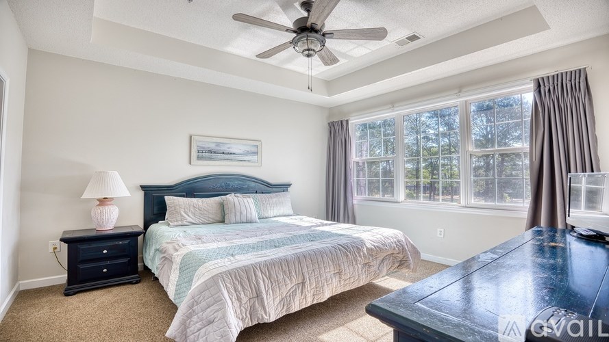 A bedroom with a bed, a ceiling fan, and a window with curtains.