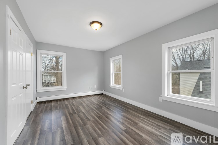 A room with a white door, grey walls, and a window with a view of a house and trees.