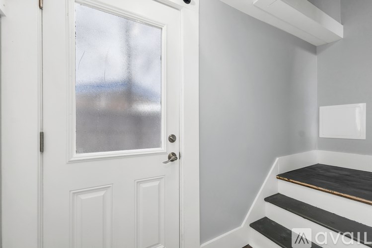 A white door with a glass window is on the left and a staircase with black steps and a white railing is on the right.