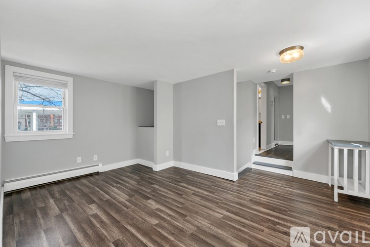 A spacious room with wood flooring and a white crib in the corner.