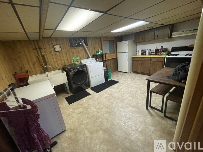 A room with a washing machine, a fridge, and a table.