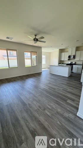 A spacious kitchen and living room with wood flooring and a ceiling fan.