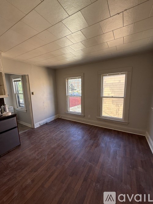 A room with wooden flooring and two windows.