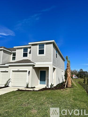 A two-story house with a garage and a palm tree in front.