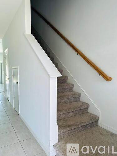 A staircase with a wooden handrail and beige carpeted steps.