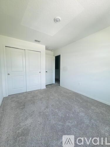 A room with grey carpet and white walls, with a door on the left and a black door on the right.