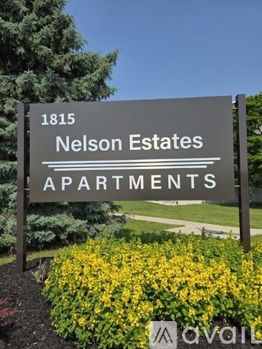 A sign for Nelson Estates Apartments is displayed in front of a flower bed.