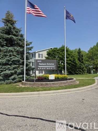 The image shows a sign for Nelson Estates Apartments with two flags on either side.