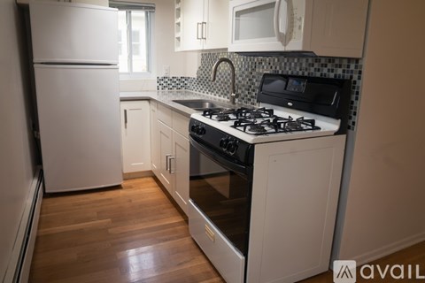 A kitchen with a white fridge, black stove, and wooden floors.