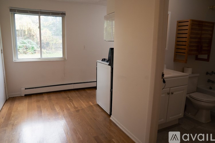 A room with a window, a radiator, a wooden floor, a white cabinet, and a white fridge.