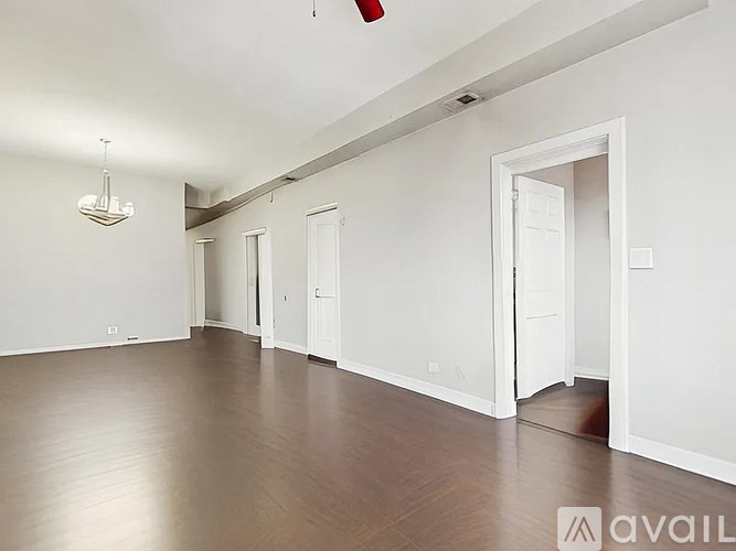 A room with white walls and wooden flooring, with a chandelier hanging from the ceiling.