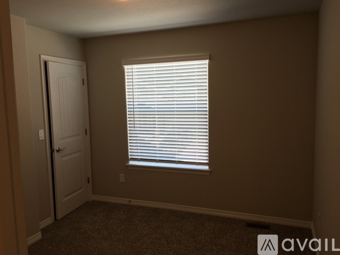 A room with a carpeted floor, a door, and a window with blinds.