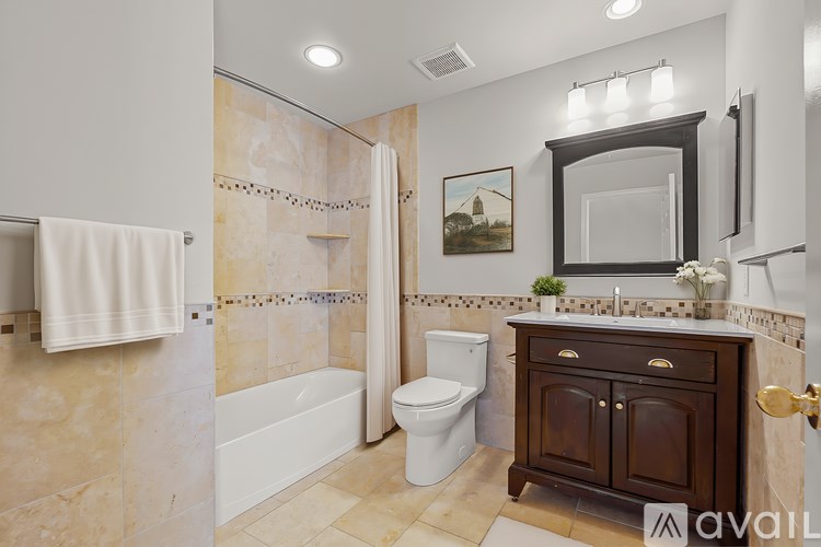 A bathroom with a white toilet, a white bathtub, a white shower curtain, a wooden cabinet, and a framed picture on the wall.