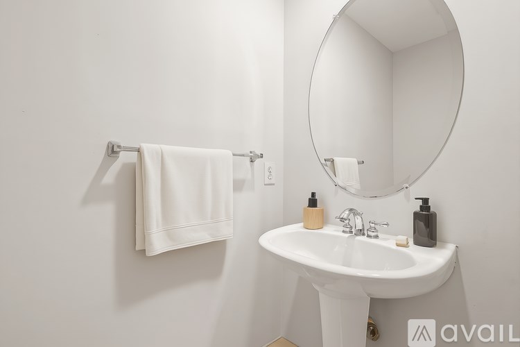 A white bathroom with a round mirror and a white sink.