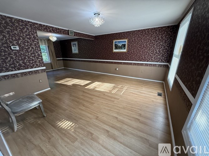 A room with wooden flooring and a wallpapered wall with a framed picture hanging on it.