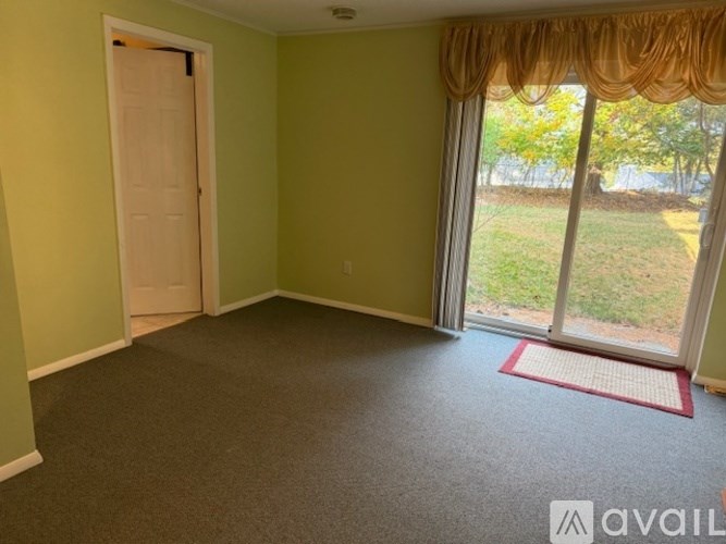 A room with a carpeted floor, a door, and a window with a view of the outdoors.