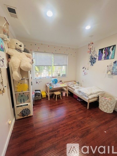 A room with wooden floors and a white wall with a teddy bear on a shelf.
