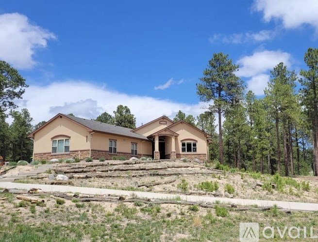 A house with a brown roof and beige walls is surrounded by trees and has a clear blue sky above it.