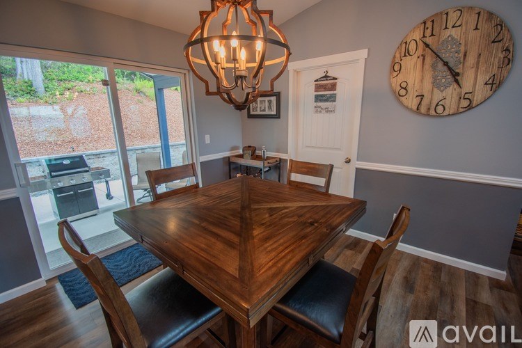 A wooden dining table with four chairs and a chandelier hangs in a room with a large clock on the wall.