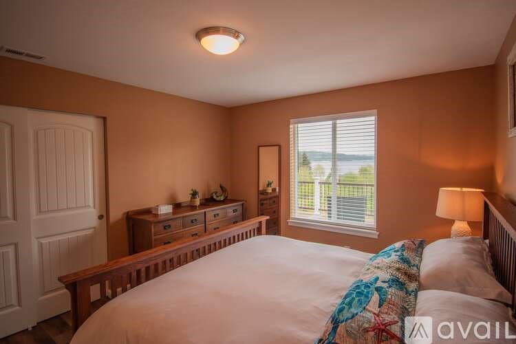 A bedroom with a large bed, a dresser, and a window with blinds.