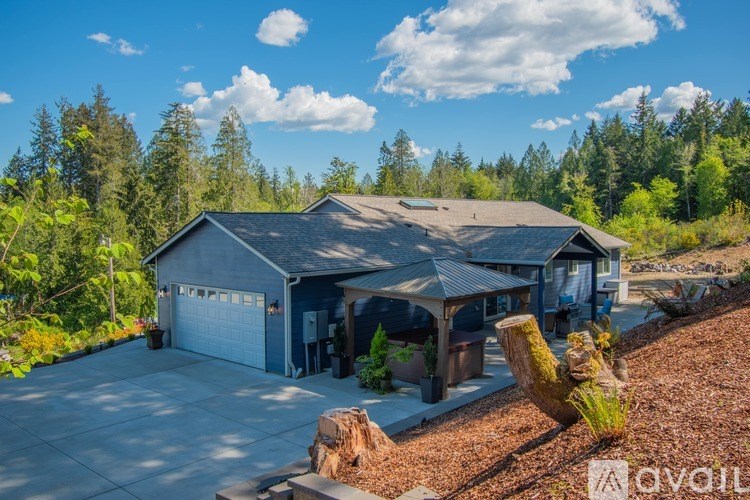 A house with a grey roof and a garage door is surrounded by trees.