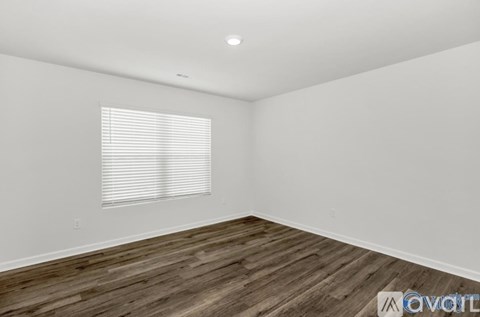 A room with wooden flooring and a window with blinds.