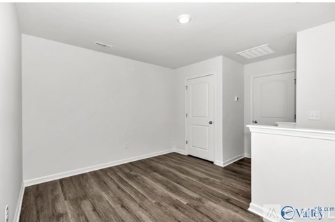 A room with white walls and wooden flooring with a door on the left and a window on the right.