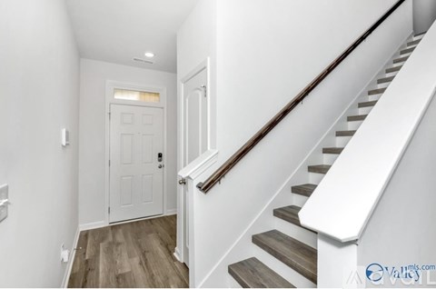 A white door is at the end of a hallway with a staircase on the right.