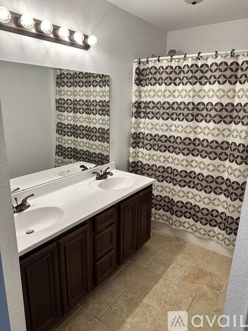 A bathroom with a shower curtain and a vanity with a sink and mirror.