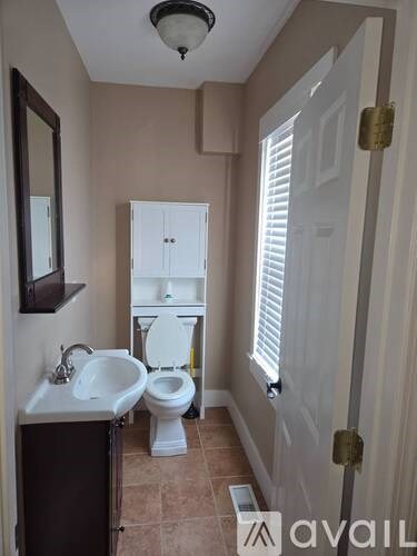 A bathroom with a toilet, sink, and cabinet.