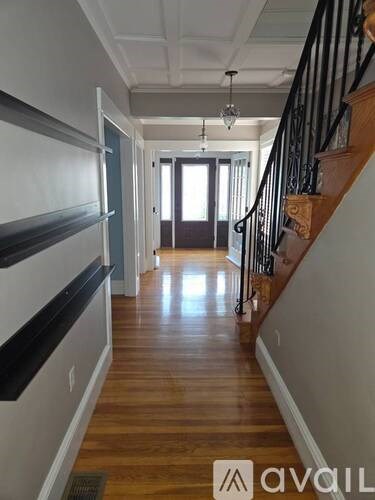 A hallway with a wooden floor and a staircase with a black railing.