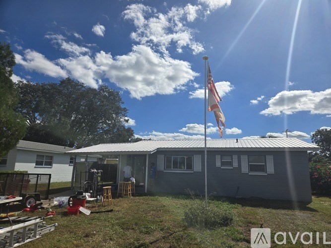A house with a metal roof and a grey exterior is surrounded by grass and trees.