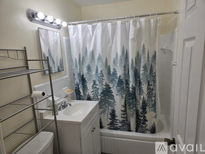 A bathroom with a white sink, toilet, and a shower curtain with trees on it.