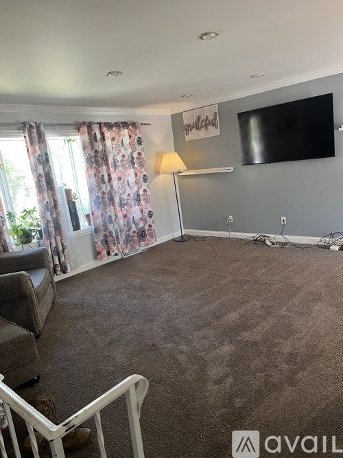 A living room with a grey carpet and a flat screen TV mounted on the wall.
