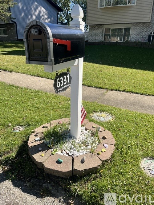 A mailbox with the number 6331 on it is mounted on a pole with a small American flag.