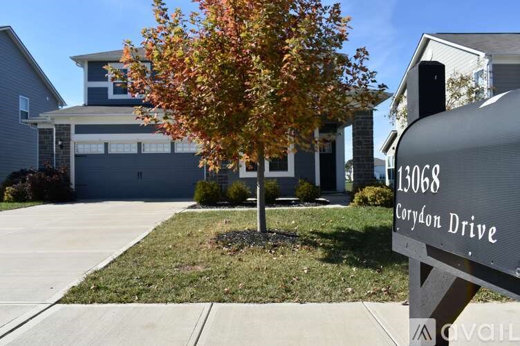A tree with orange leaves is in front of a grey house with a sign that says Corydon Drive.