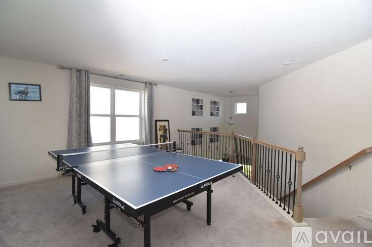 A ping pong table is in a large room with a staircase.