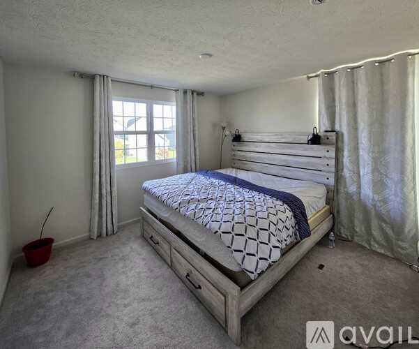 A bedroom with a large bed and a window with curtains.