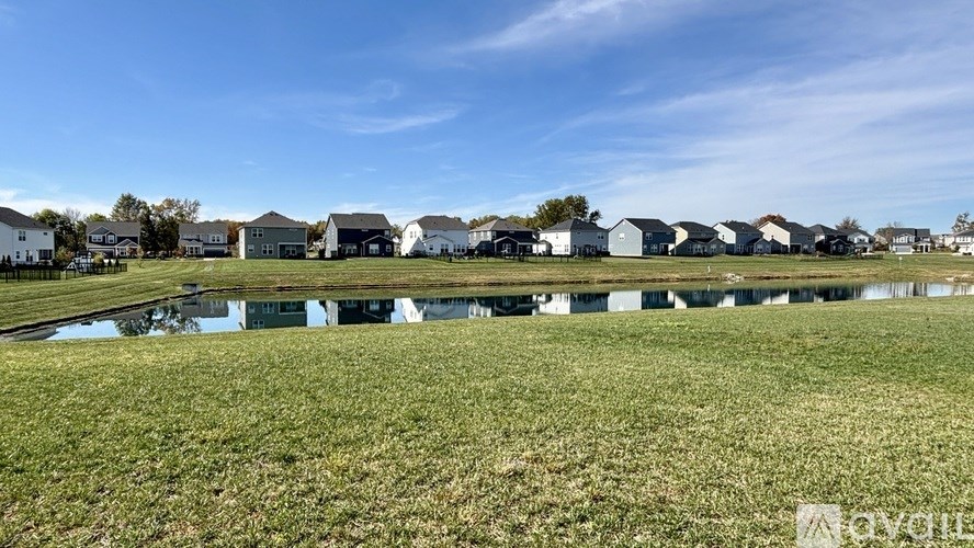 A row of houses are reflected in a pond in a grassy field.