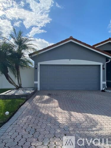 A house with a grey garage door and a brick driveway.